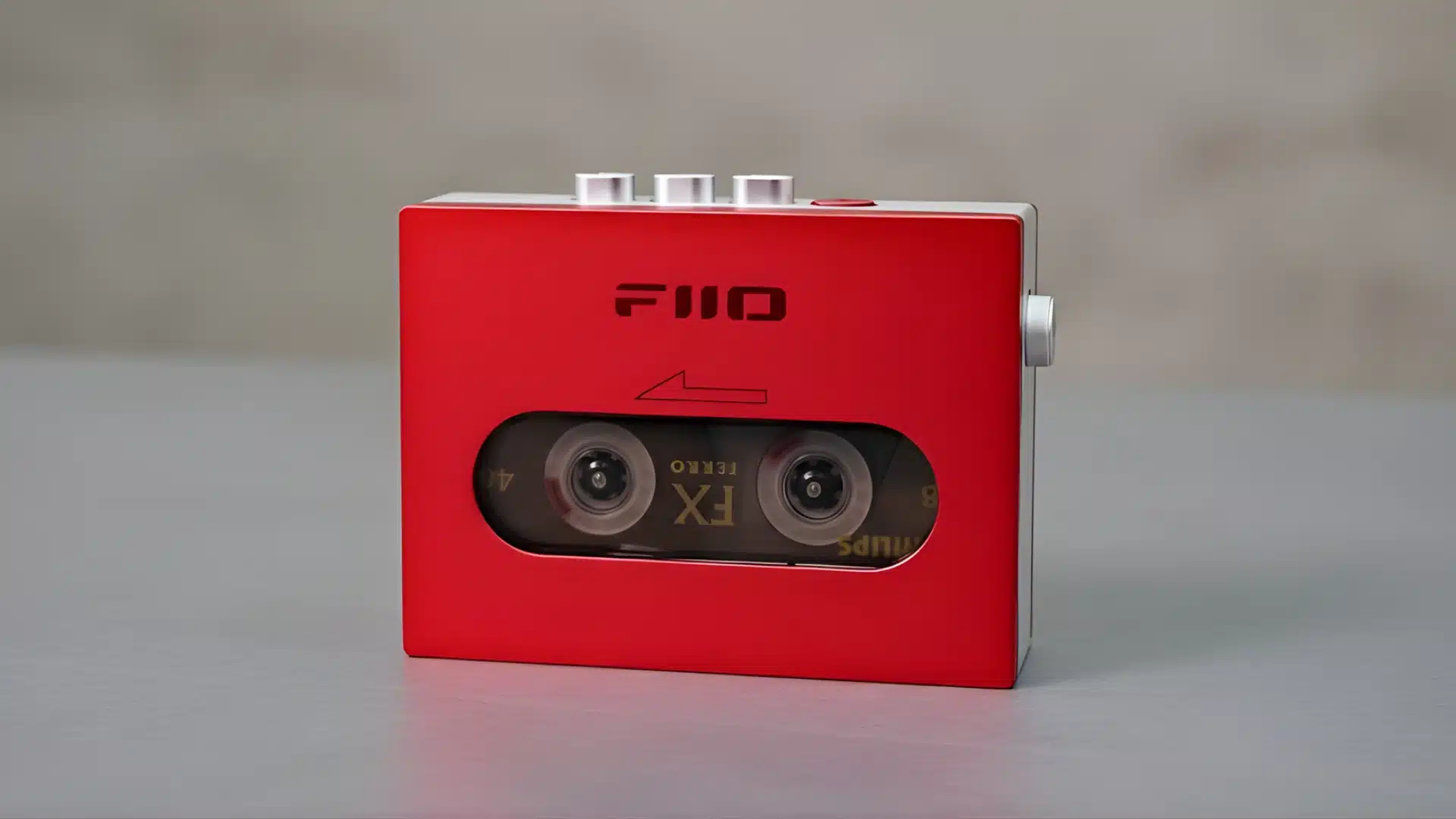 Red FiiO CP13 cassette player with tape visible through front window placed on a gray surface