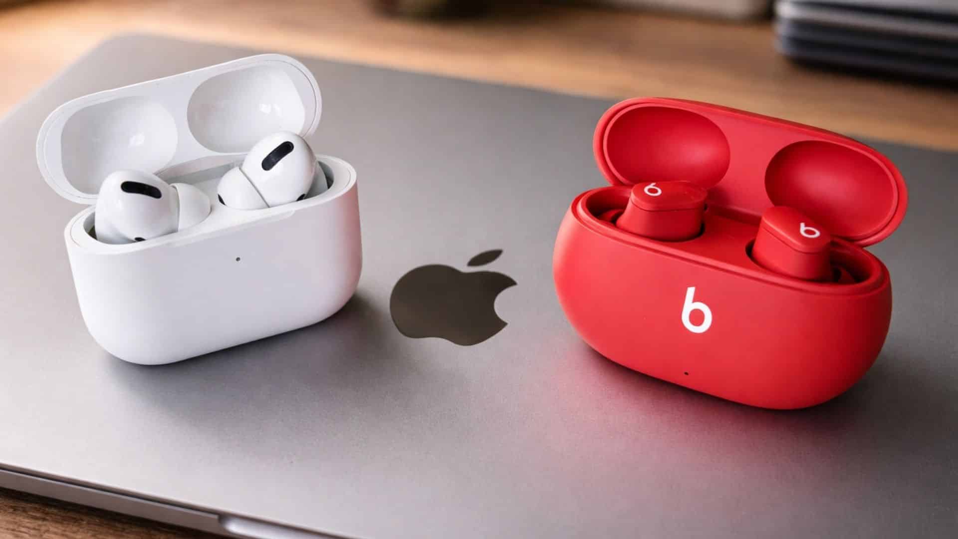 White AirPods Pro in a white case and red Beats Studio Buds in a red case sitting on a grey Apple laptop