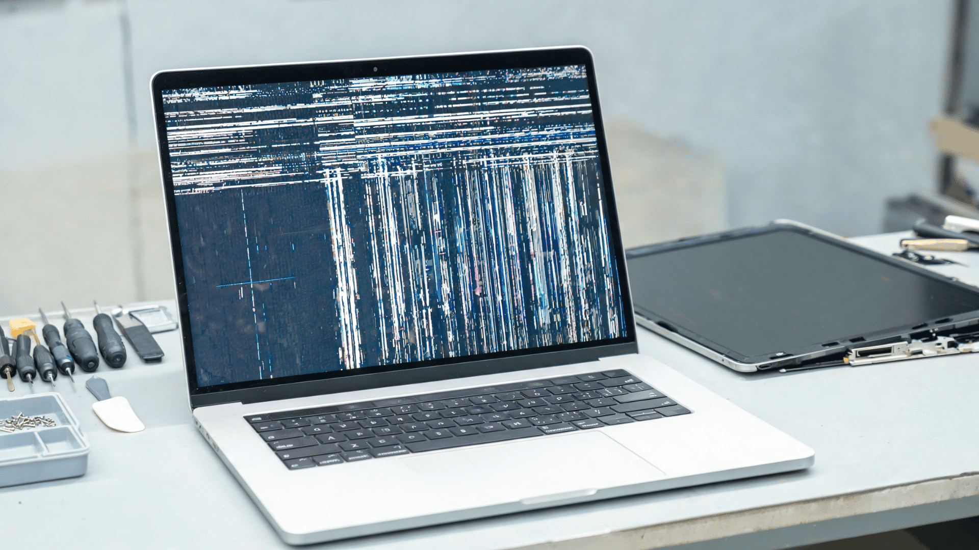 A MacBook with a cracked screen sits on a wooden table, highlighting screen damage.