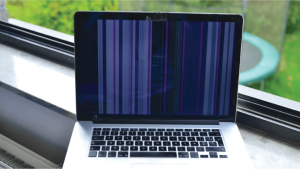 Macbook displaying a screen with vertical colored lines, positioned on a windowsill.