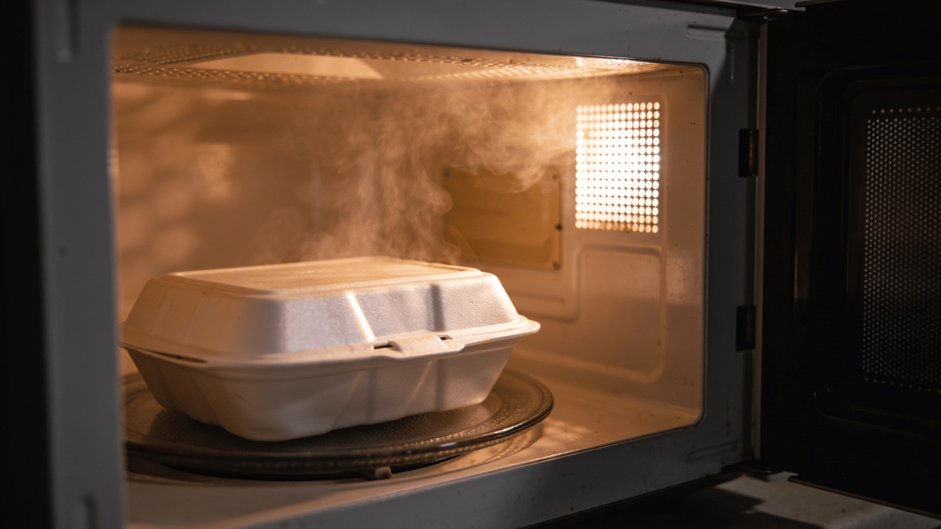 Styrofoam food container inside a microwave oven with steam visible