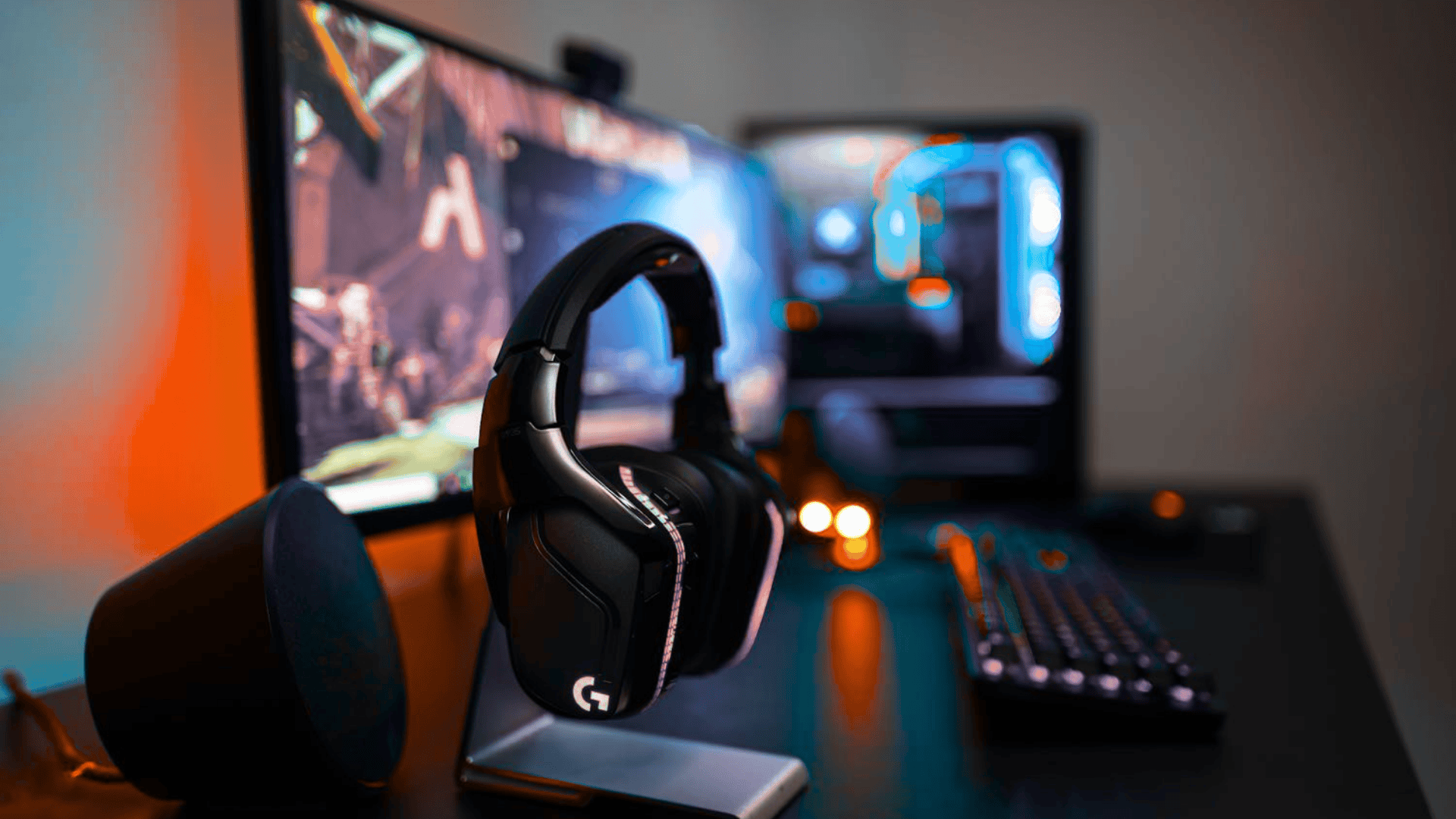 Logitech G935 wireless gaming headset on a gaming setup with monitor and keyboard background.
